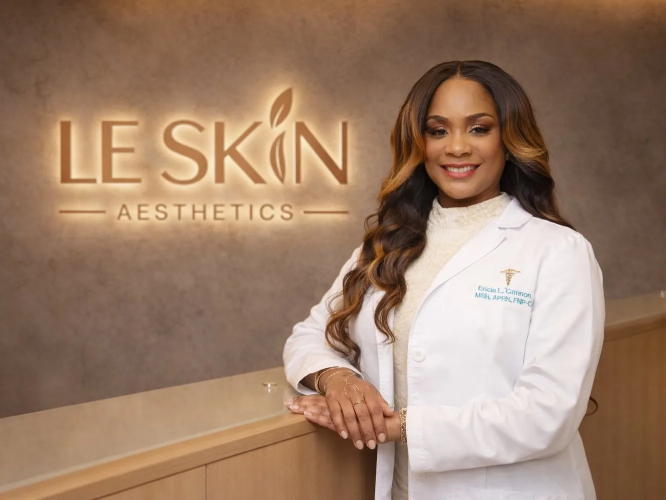 Ericia L. Cannon, MSN, APRN, FNP-C, smiling at the Le Skin Aesthetics reception desk in front of the lit clinic sign